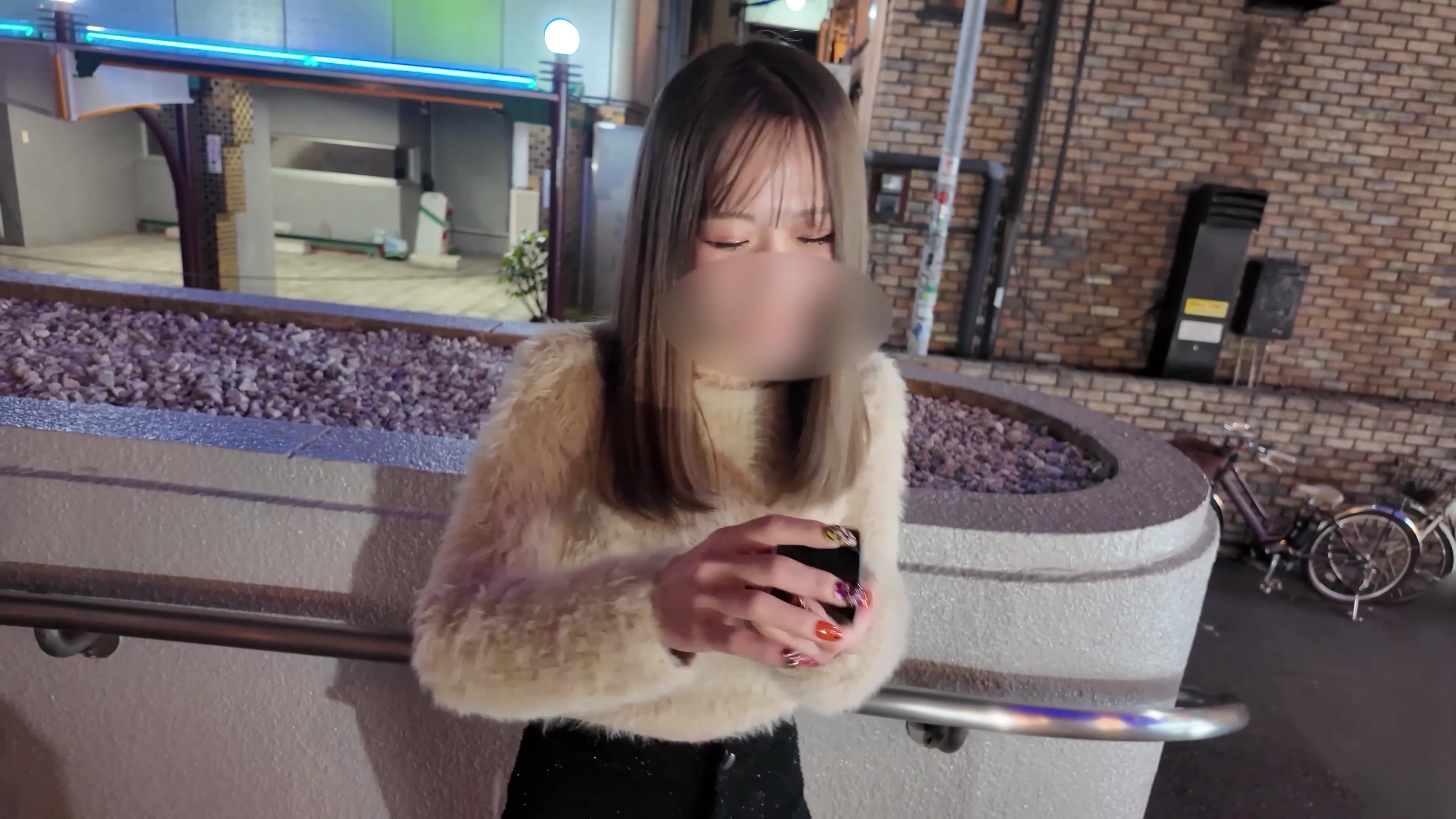 A performer in a cream fuzzy sweater standing on a city street at night, a clothed still from a video on this page
