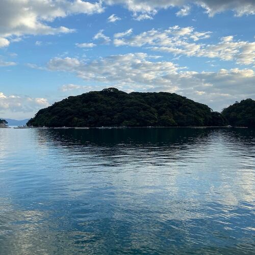 Calm sea and a wooded island under a partly cloudy sky