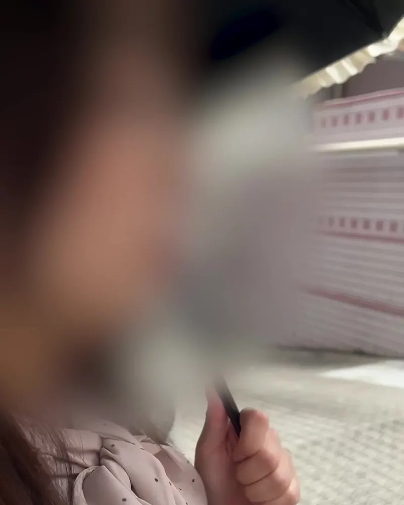 A woman in a dotted blouse holding an umbrella outdoors, a clothed still from a Kaede video (face blurred in the original)