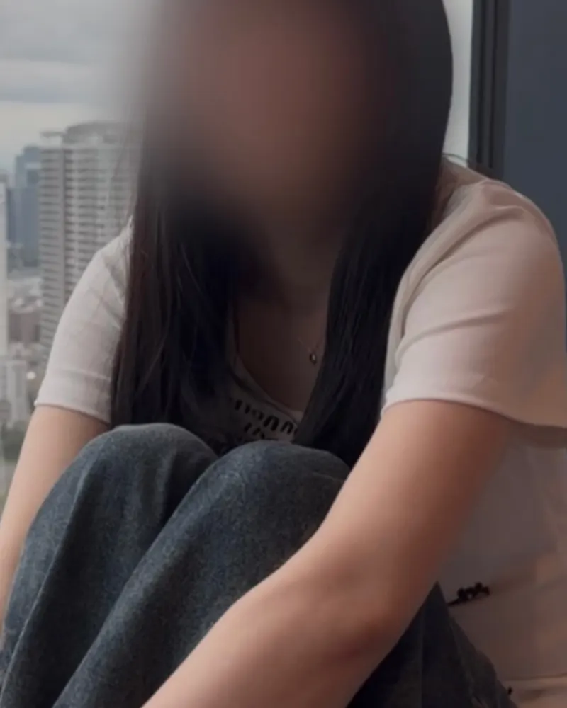 Clothed still from a video by kaito: a woman in a T-shirt and jeans by a window, face blurred