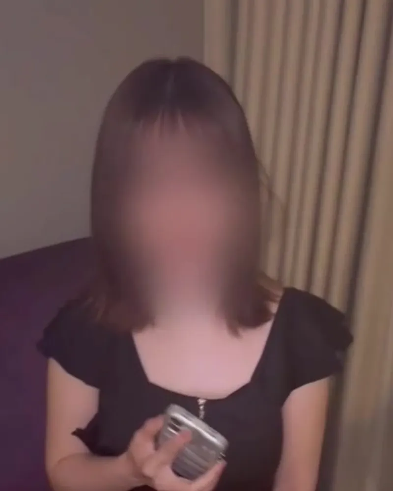 Clothed still from a video by kaito: a woman in a black dress holding a phone, face blurred