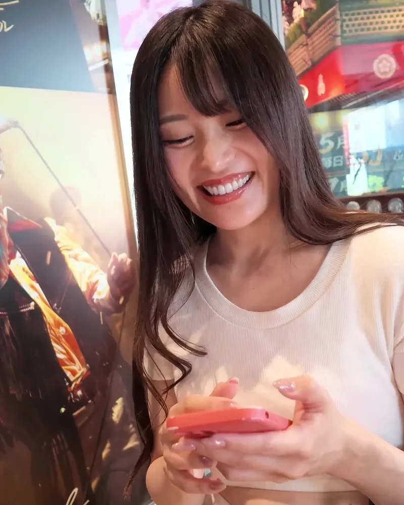 A performer in a white knit top laughing while looking at a phone, a clothed still from a video on this page