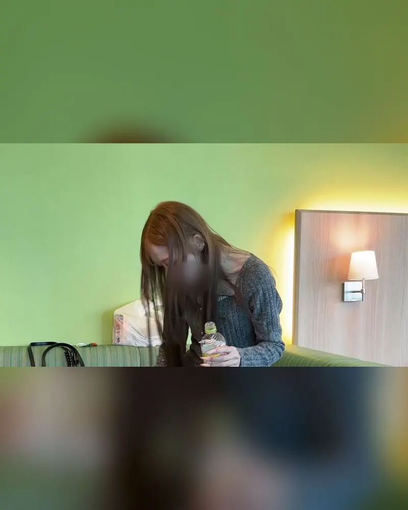 A woman in a grey knit sweater holding a water bottle, a clothed still from a Name-inu video (face blurred in the original)