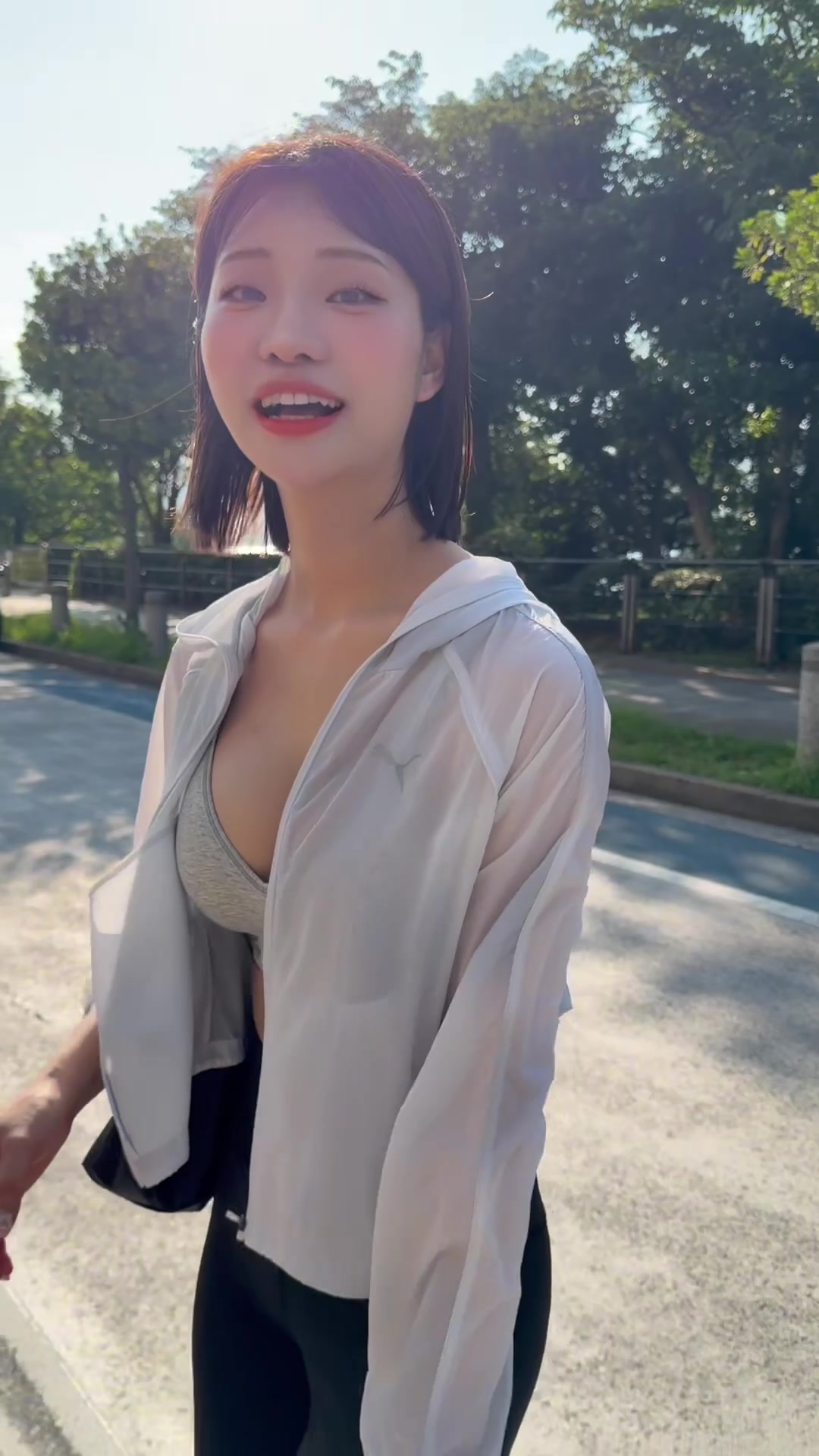 A performer in a white zip-up jacket smiling outdoors, an unedited still from a Retsu video