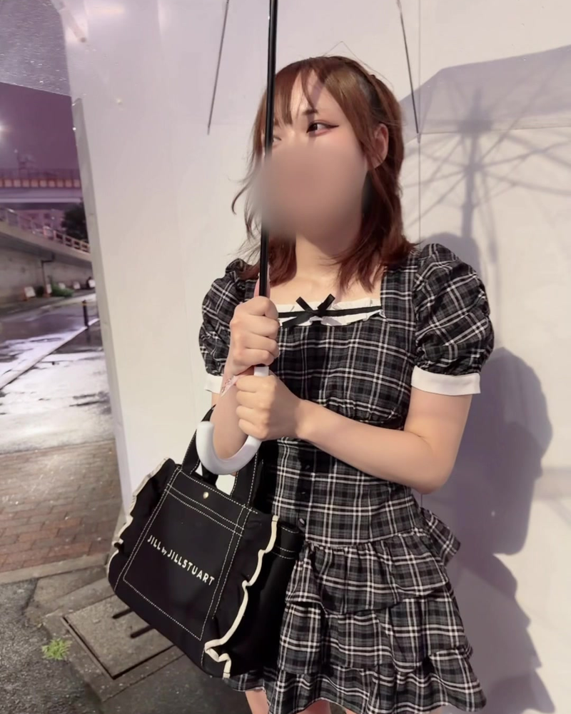 Clothed still from a video by Shinnosuke: a woman in a checked dress holding an umbrella on a rainy street, face blurred